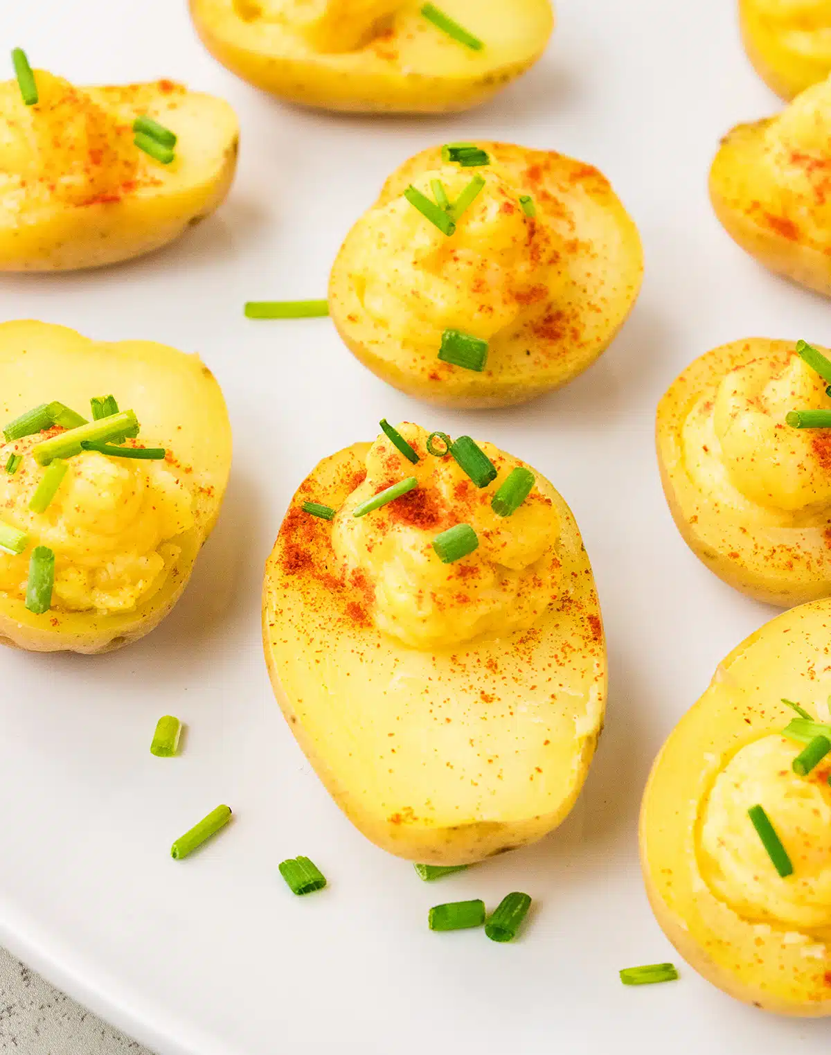 Small potatoes with a creamy filling on a white background. There are chives scattered accross them.