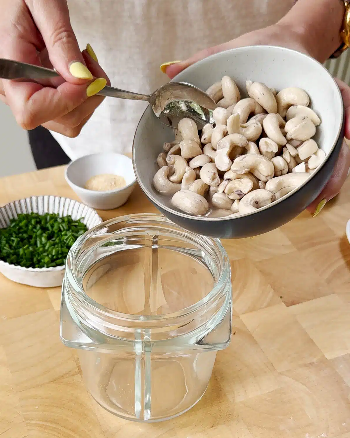 Showing adding the drained soaked cashews and other ingredietns to a blender bowl.