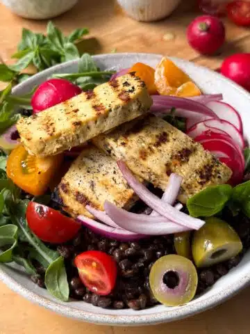 A bowl of lentils with various toppings such as tomatoes, greens and olives on top.
