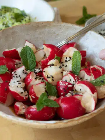 A bowl of smashed radish salad ready to eat. There is a fork picking up a piece of radish.