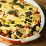 A baking pan of gnocchi and lentil bake topped with pesto that has just come out of the oven.
