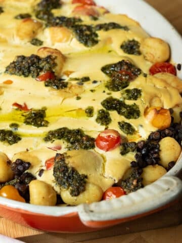 A baking pan of gnocchi and lentil bake topped with pesto that has just come out of the oven.