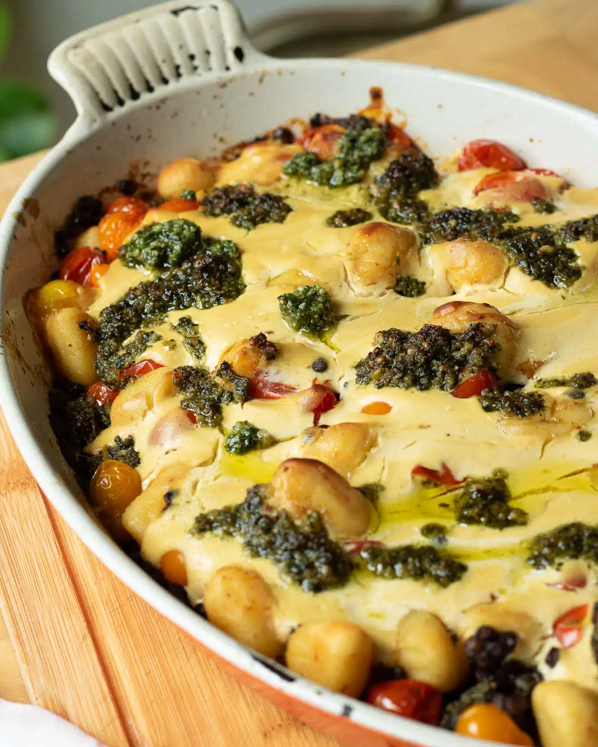 A baking pan of gnocchi and lentil bake topped with pesto that has just come out of the oven. 