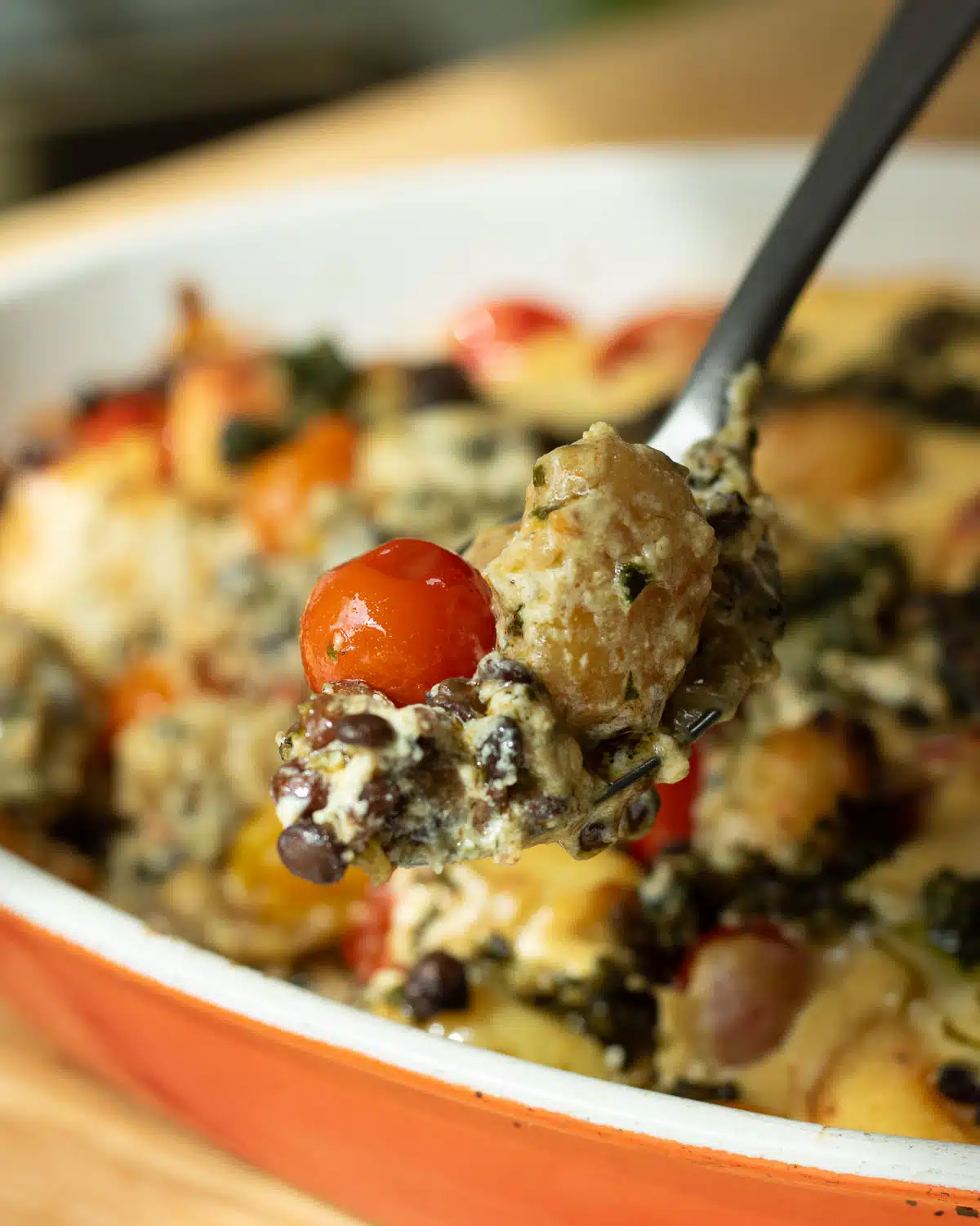 A spoon showing the texture of the gnocchi and creamy cheese with a tomato and lentils once it is baked.