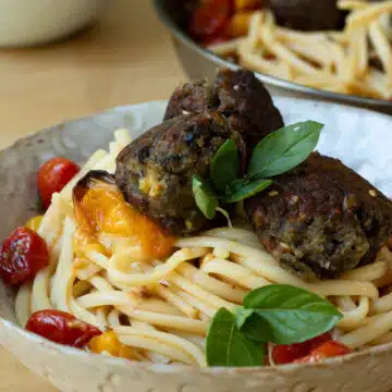 A pile of spaghettie with lentil and aubergine meatballs on top of it. There is another pan in the background.