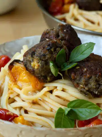 A pile of spaghettie with lentil and aubergine meatballs on top of it. There is another pan in the background.