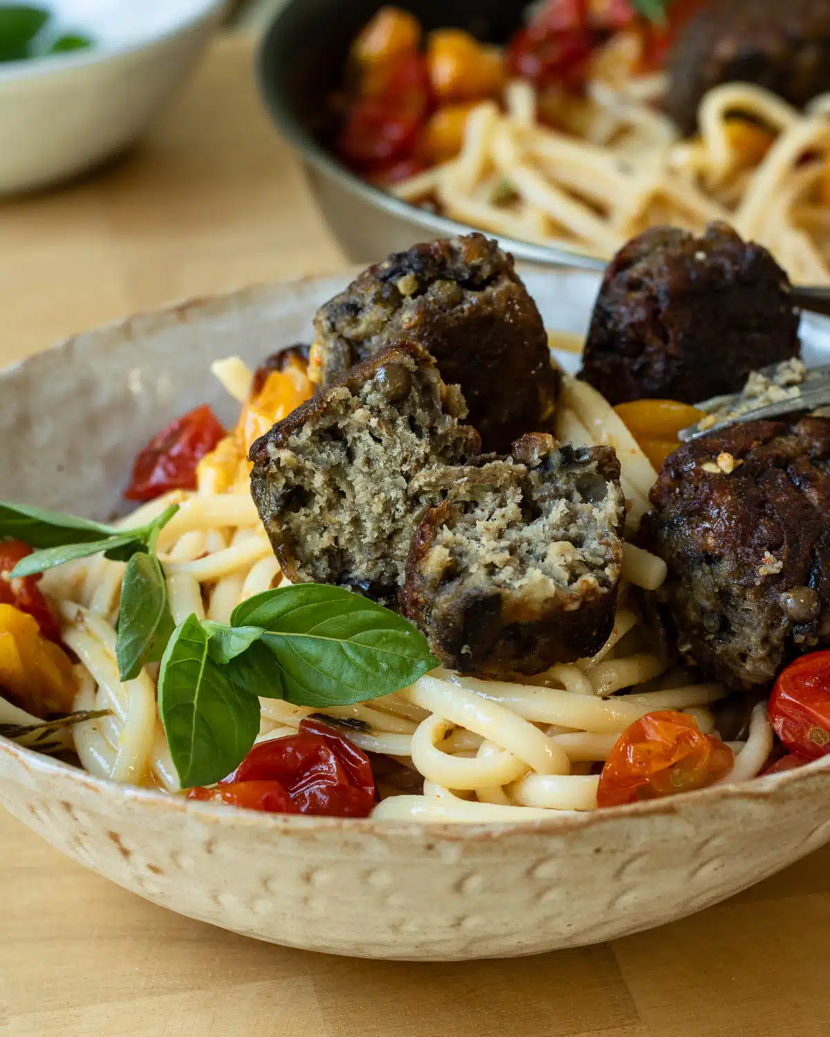 Three lentil and eggplant meatballs on top of spaghetti. One of the meatballs is broken open to show the texture inside.
