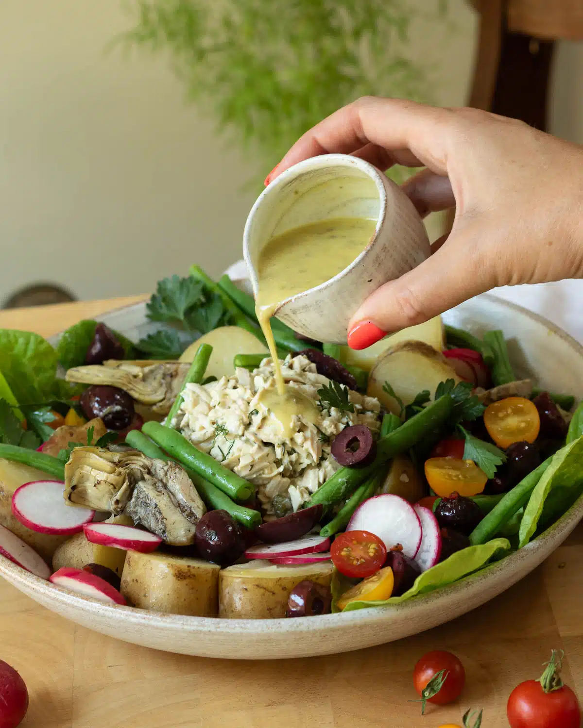 A hand is pouring a vinaigrette salad dressing over a plate of vegan nicoise salad.