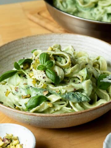 A bowl of lemon basil zucchini pasta ready to eat with a pan of the pasta in the background.