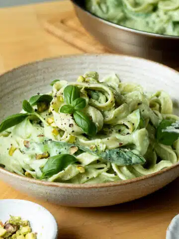 A bowl of lemon basil zucchini pasta ready to eat with a pan of the pasta in the background.