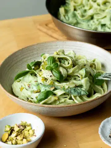 A bowl of lemon basil zucchini pasta ready to eat with a pan of the pasta in the background.