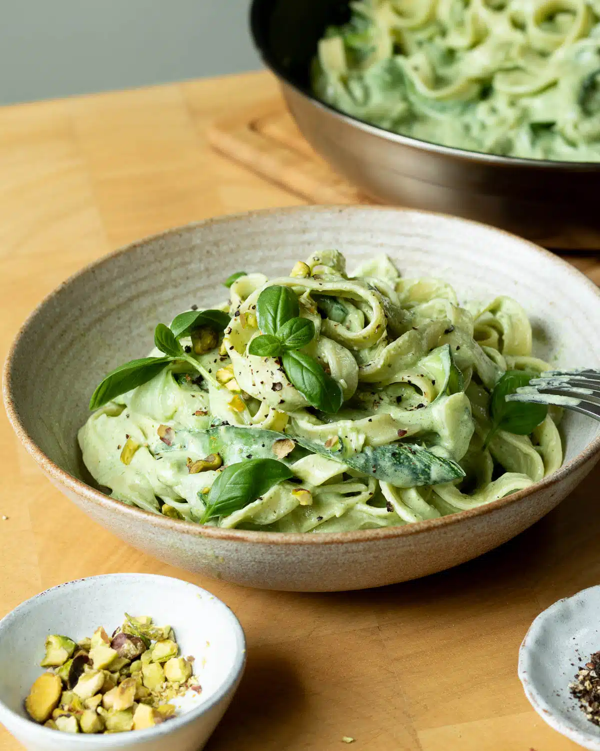 A bowl of lemon basil zucchini pasta ready to eat with a pan of the pasta in the background.