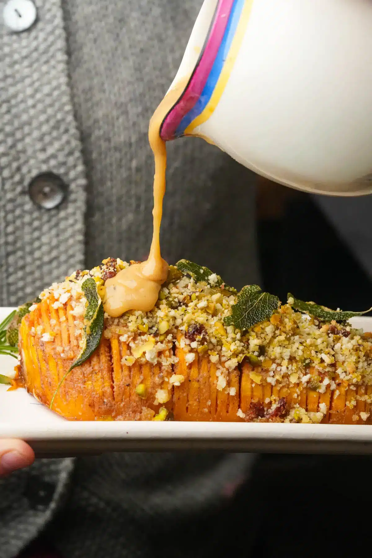 A hasslebacked squash with crunchy topping and a miso dressing being poured over it.