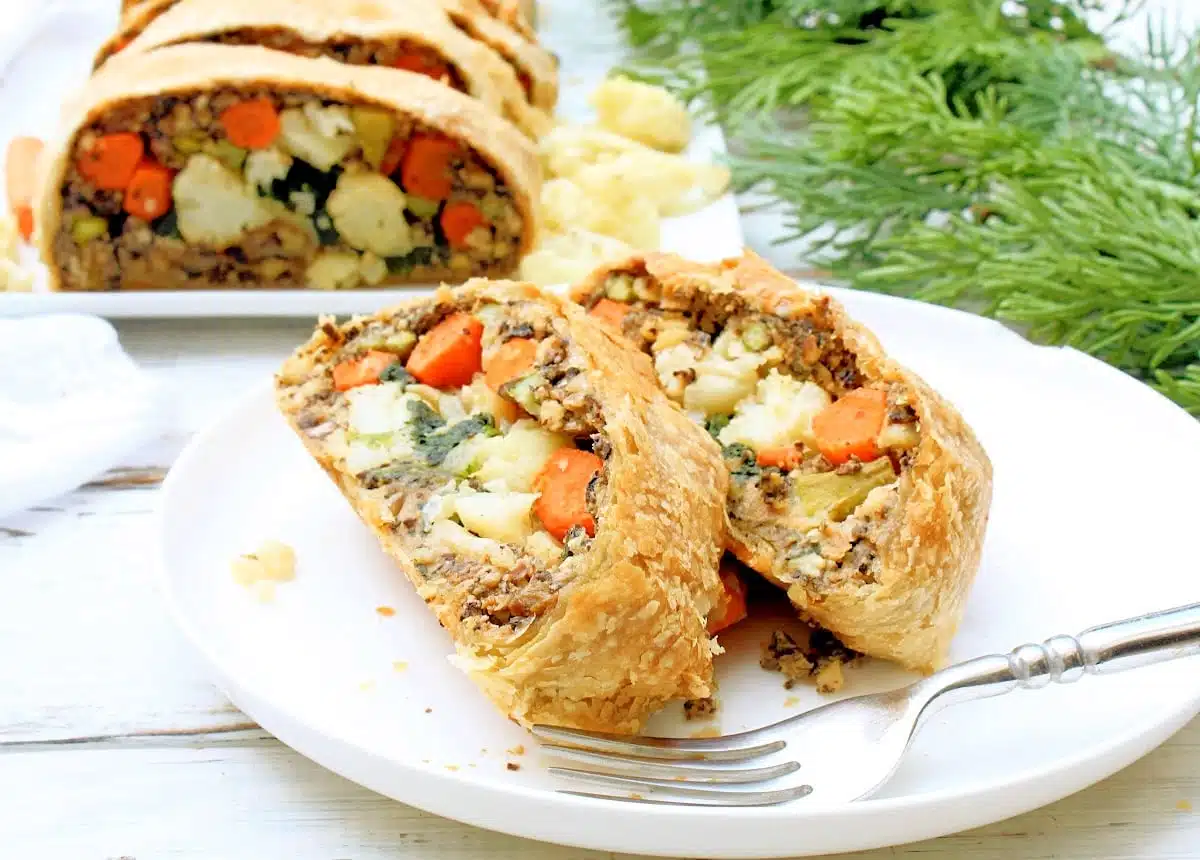 Wellington stuffed with roasted vegetables with two slices on a plate in front of it.