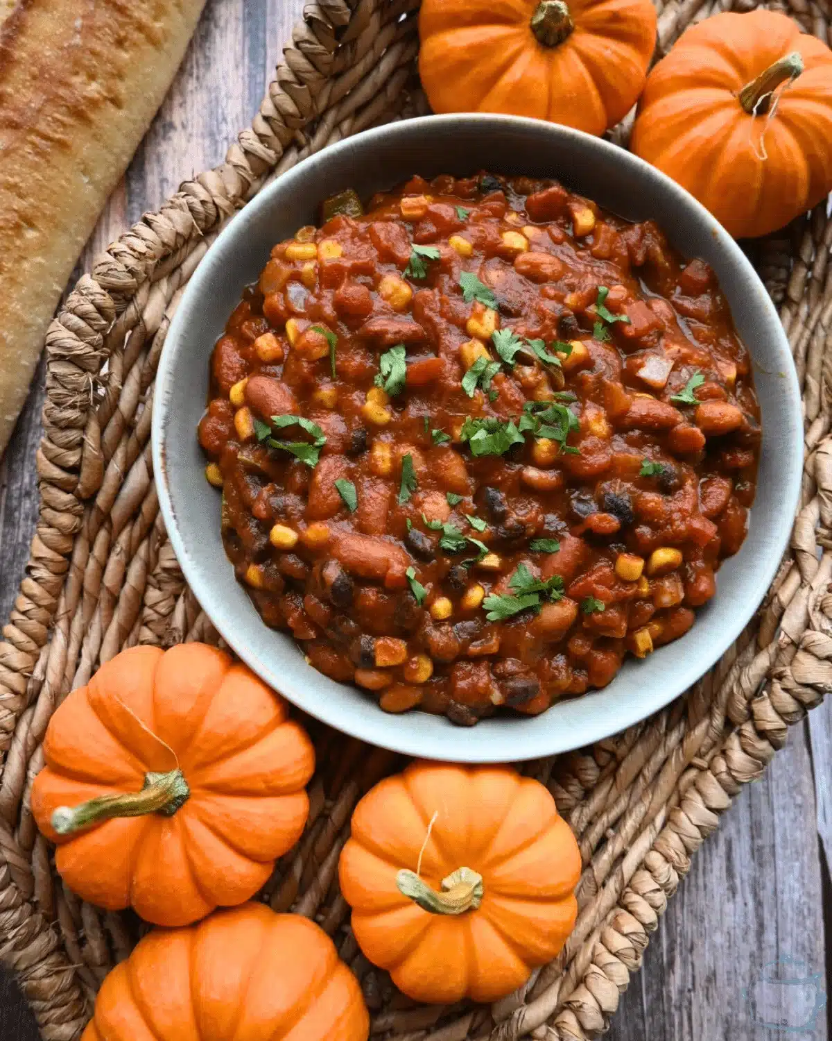 A bowl of pumpkin bean chili ready to eat. There are some mini pumpkins next to it.