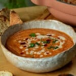 A bowl of roasted sweet potato and red lentil soup with a tahini harissa drizzle on top in a bowl ready to serve.