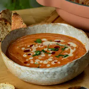 A bowl of roasted sweet potato and red lentil soup with a tahini harissa drizzle on top in a bowl ready to serve.