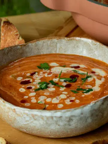 A bowl of roasted sweet potato and red lentil soup with a tahini harissa drizzle on top in a bowl ready to serve.