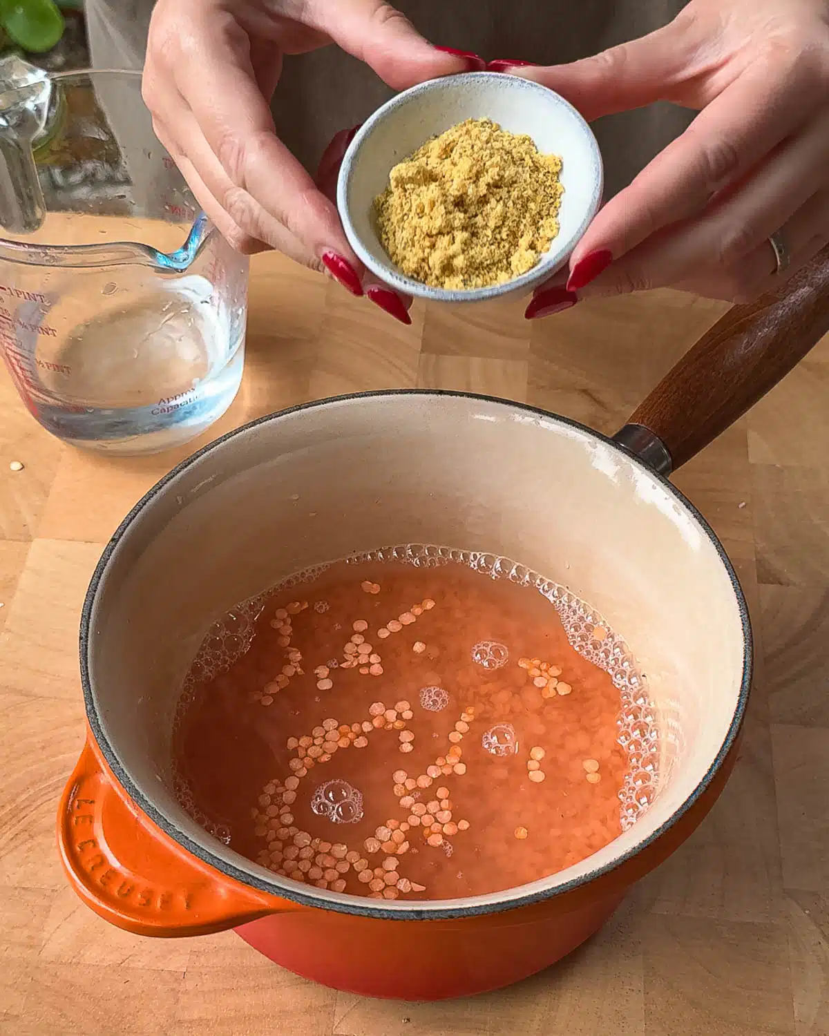 A small pot with lentils and water in it, and vegan boullion stock powder is being added to the pot before boiling.