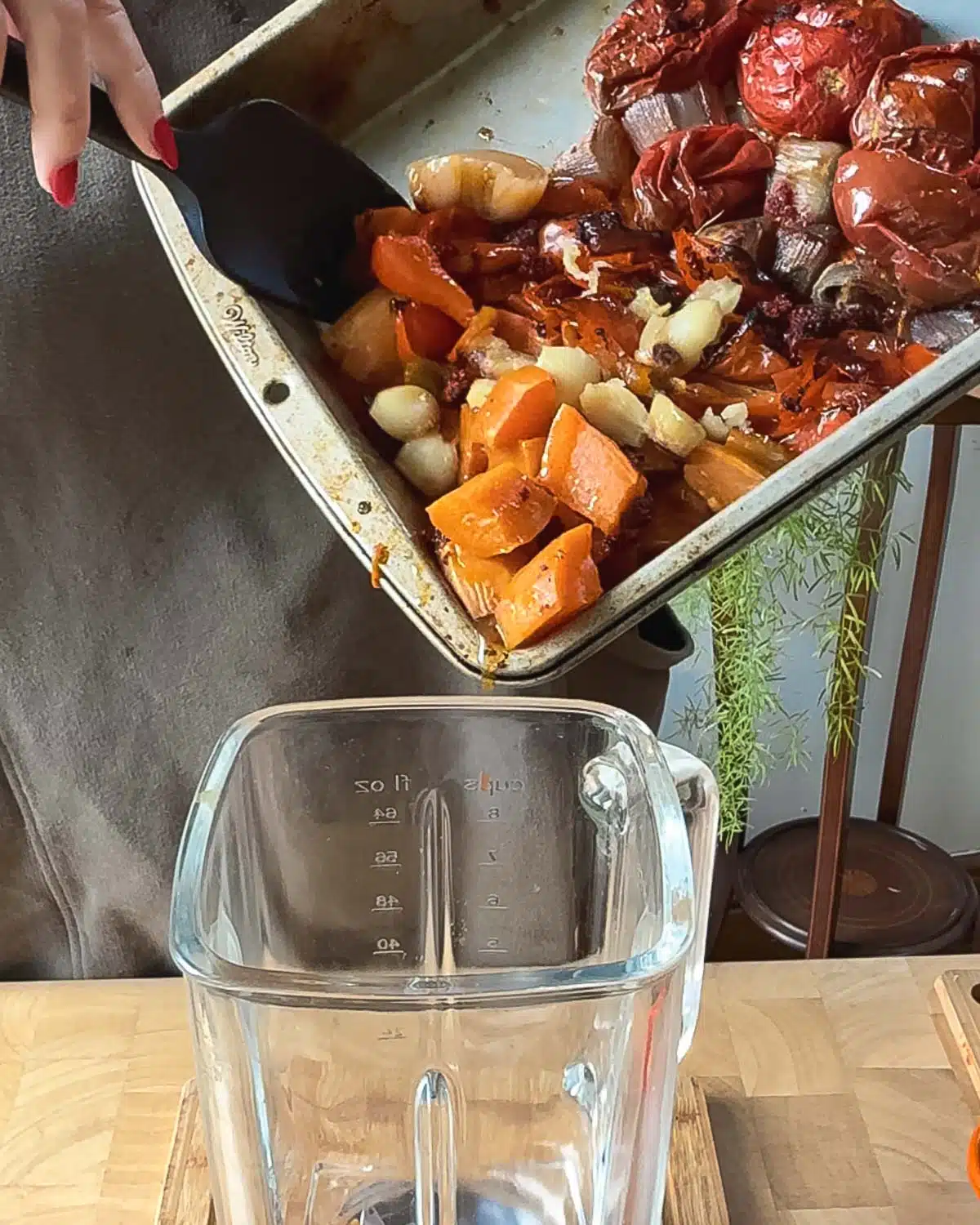Showing a blender with the roasted vegetables being spooned into it.
