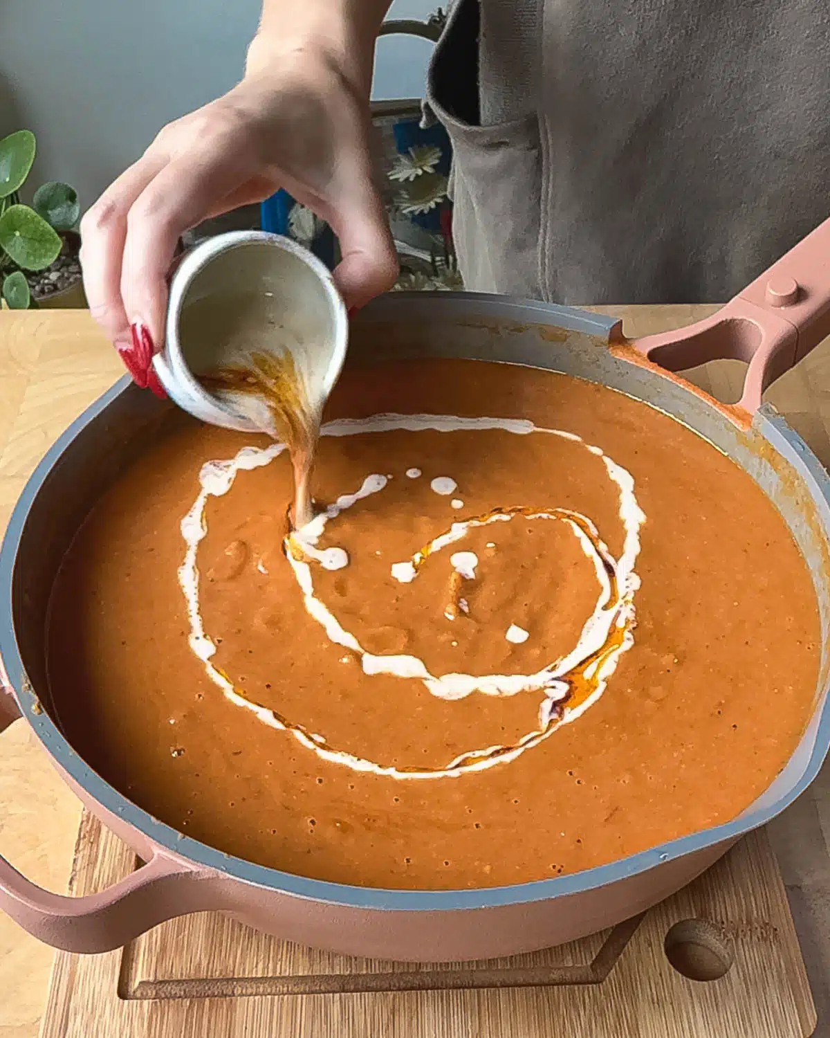 A pan of hot soup ready to eat being dressed with some tahini cream and harissa oil.
